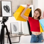 Influenciadora jovem mostrando sacolas de compras diante de uma câmera, representando o comportamento do consumidor híbrido