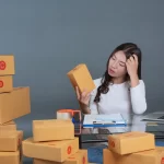 Mulher analisando caixas de produtos enquanto tenta organizar estoque, mostrando dificuldade em prever rupturas