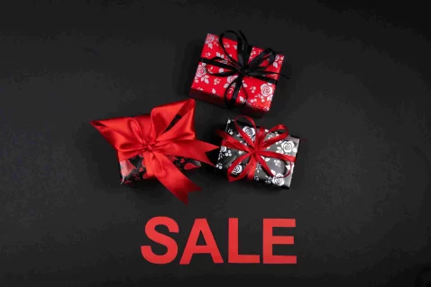 Pacotes de presente vermelhos e pretos com laços sobre fundo escuro e a palavra SALE em destaque, representando ofertas combinadas no Natal.