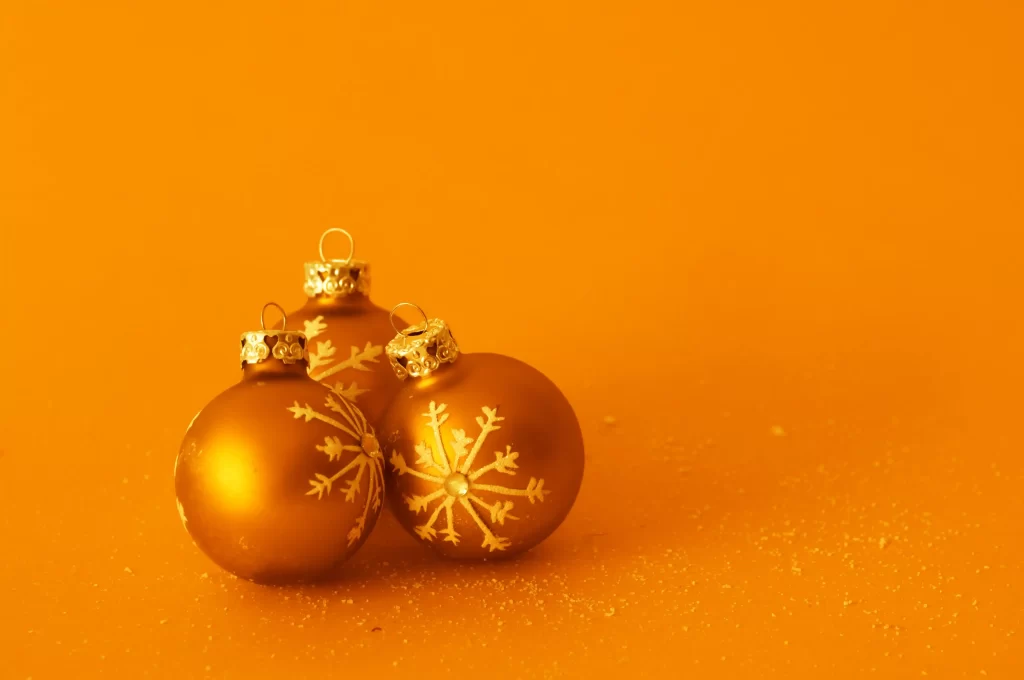 Três bolas natalinas douradas com detalhes de flocos de neve sobre fundo laranja