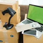 Caixas de envio, laptop e leitor de código de barras sobre a mesa, simbolizando operações afetadas pelo pico de devoluções