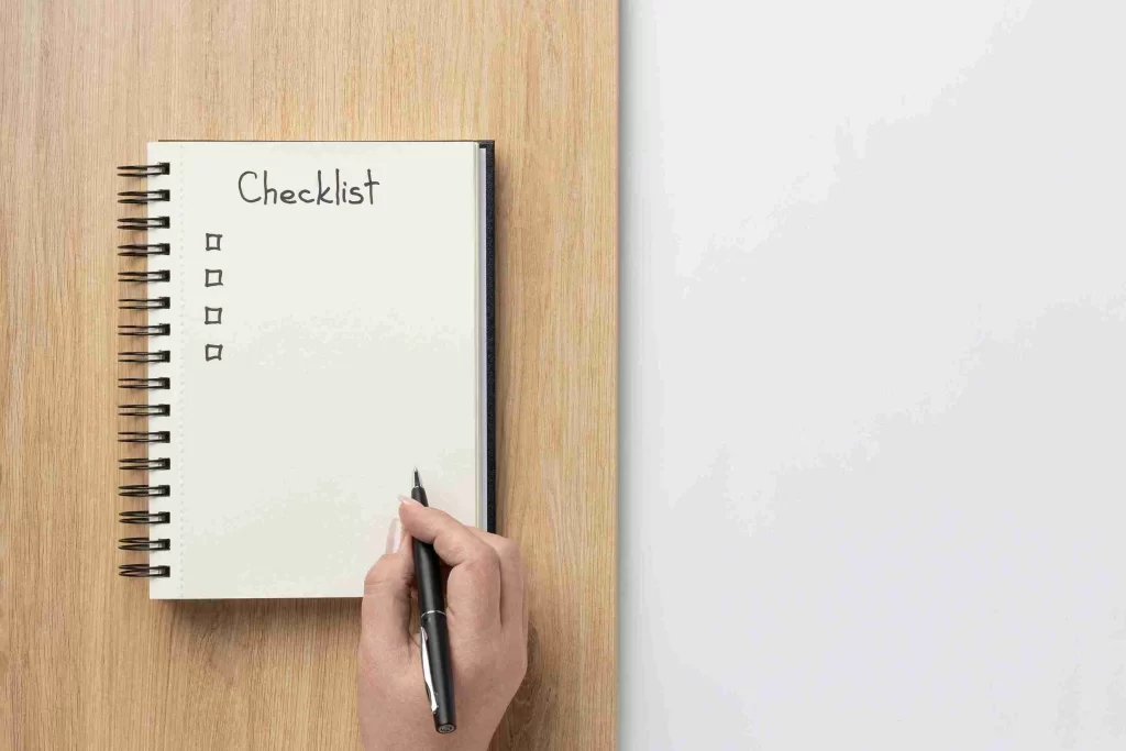 Foto vista de cima de um caderno aberto sobre uma mesa de madeira. Na página está escrito “Checklist” à mão, com quatro quadrados vazios abaixo