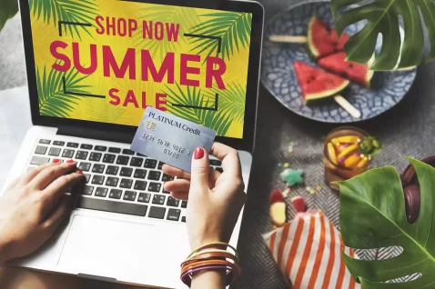 Pessoa comprando online em promoção de verão exibida no notebook, com ambiente tropical ao redor