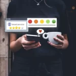 Pessoa em pé segurando um celular em uma mão e uma xícara de café na outra, enquanto ícones de avaliação com estrelas e carinhas de satisfação aparecem sobre a tela