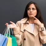 Mulher com sacolas de compras olhando pensativa, representando um consumidor cauteloso antes de finalizar compras online