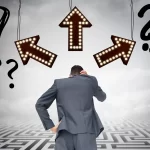 Homem de terno visto de costas, com a mão na cabeça, parado diante de três setas iluminadas apontando para direções diferentes