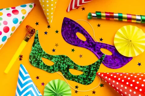 Conjunto de acessórios para Carnaval sobre fundo amarelo, com máscaras coloridas, chapéus de festa, apitos, confetes e serpentinas