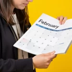 Mulher segurando calendário aberto em fevereiro de 2026 sobre fundo amarelo, representando planejamento e comportamento consumidor no início do ano