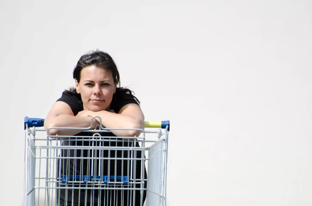 Mulher encostada em um carrinho de compras vazio, com expressão reflexiva, simbolizando cautela e indecisão no processo de compra