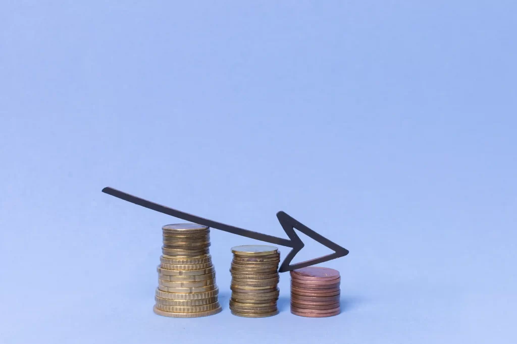 Pilhas de moedas de diferentes tamanhos com seta apontando para baixo, simbolizando redução de lucro