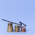 Pilhas de moedas de diferentes tamanhos com seta apontando para baixo, simbolizando redução de lucro
