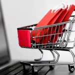 Mini carrinho de compras com sacolas vermelhas sobre teclado de notebook, simbolizando vendas em marketplace vertical