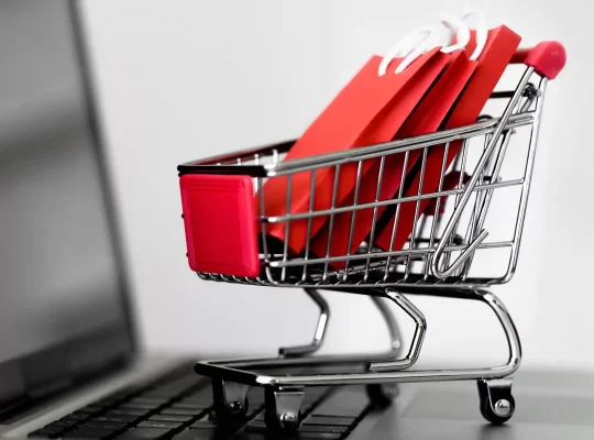 Mini carrinho de compras com sacolas vermelhas sobre teclado de notebook, simbolizando vendas em marketplace vertical