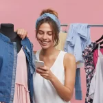 Mulher analisando roupas e usando celular em ambiente de loja, representando o crescimento do mercado de moda e-commerce em 2026.