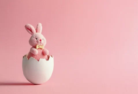 Coelho de pelúcia rosa dentro de casca de ovo branca sobre fundo rosa, representando ideias sobre o que vender na Páscoa além de chocolate