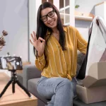 Mulher sorrindo grava vídeo mostrando roupa retirada de caixa, simbolizando criação de conteúdo e venda de produto viral e-commerce nas redes sociais