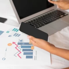 Pessoa analisando gráficos de desempenho no laptop e smartphone para avaliar dados de visitas e tendências de vendas online