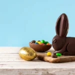 Coelho de chocolate com ovos e doces sobre mesa representando produtos de Páscoa e risco de estoque parado após a data