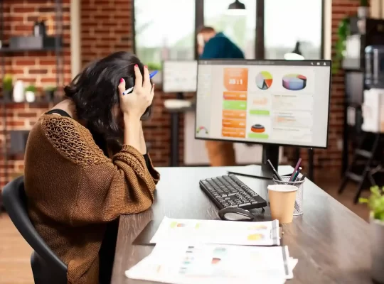 Profissional sentado diante de computador analisando gráficos com expressão preocupada, representando desafios de margem no Mercado Livre