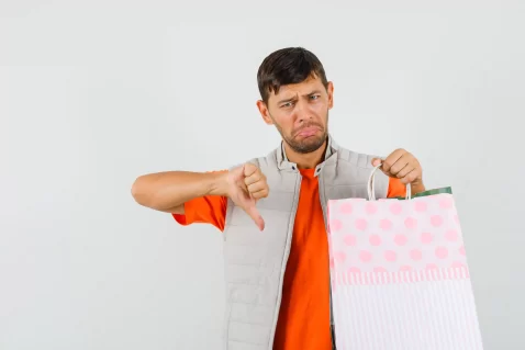 Homem segurando sacola de compras e fazendo sinal negativo com o polegar, representando erros internos que prejudicam o posicionamento no Mercado Livre