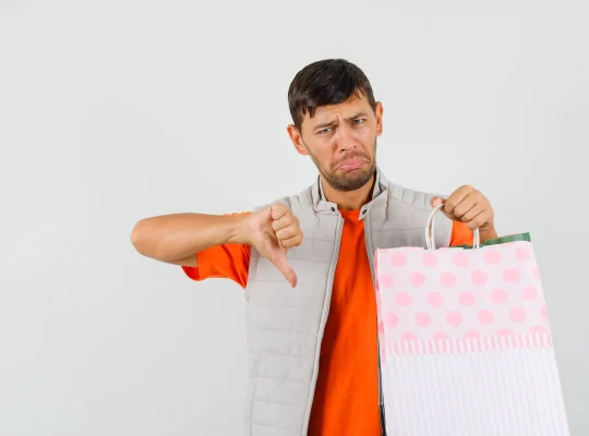 Homem segurando sacola de compras e fazendo sinal negativo com o polegar, representando erros internos que prejudicam o posicionamento no Mercado Livre