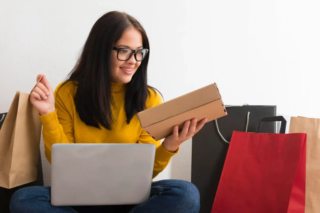 Mulher comprando online com notebook e sacolas, representando estratégia de produto de entrada no e-commerce para aumentar vendas