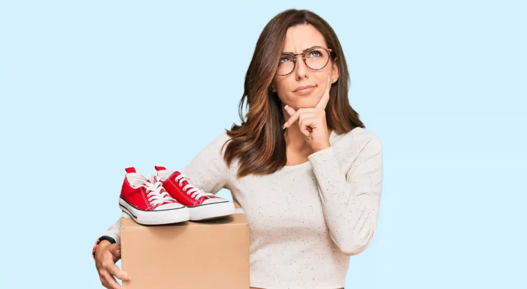 Mulher analisando tênis sobre caixa de envio, representando avaliação de produtos baratos para vender com potencial de lucro