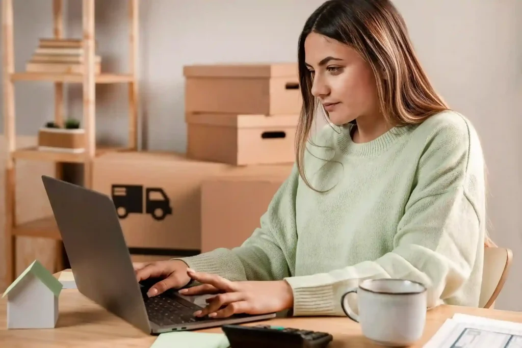 Mulher trabalhando no notebook cercada de caixas de envio, representando gestão de produtos para vender online