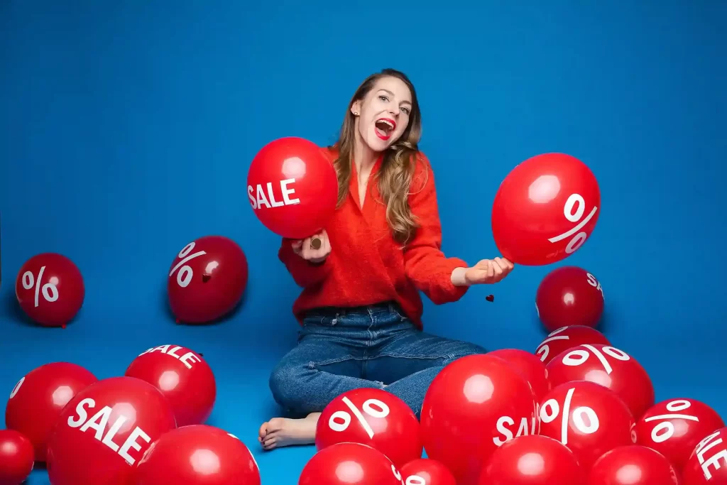 Mulher segurando balões com palavras “sale” e símbolo de porcentagem representando promoções e descontos no e-commerce