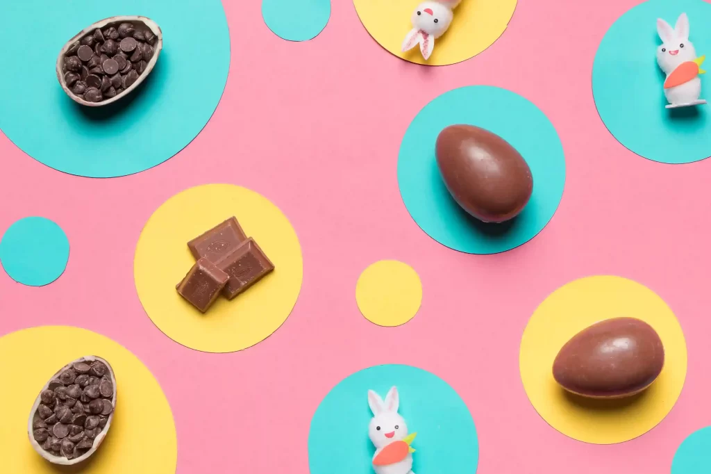 Ovos de chocolate, pedaços de chocolate e pequenos coelhos decorativos sobre fundo colorido, representando tendências e microtendências de produtos para Páscoa 2026