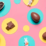 Ovos de chocolate, pedaços de chocolate e pequenos coelhos decorativos sobre fundo colorido, representando tendências e microtendências de produtos para Páscoa 2026