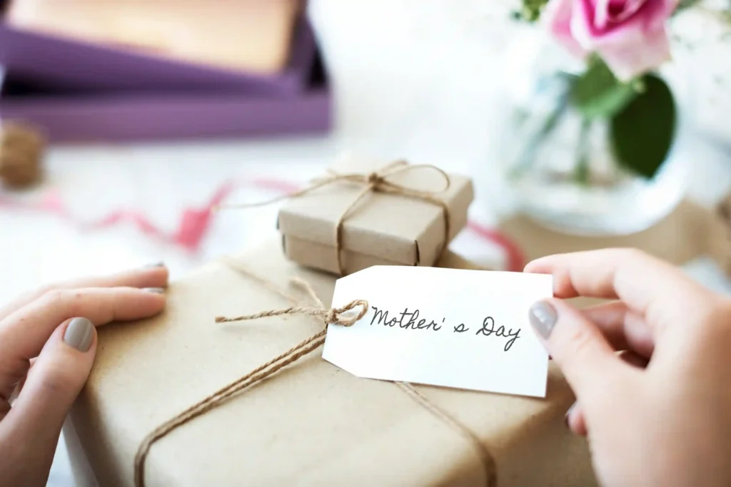 Mãos segurando etiqueta Mother's Day em presente embrulhado em papel kraft, representando a necessidade de ajustar o anúncio do Dia das Mães no Mercado Livre