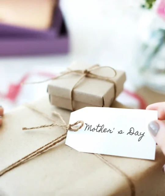Mãos segurando etiqueta Mother's Day em presente embrulhado em papel kraft, representando a necessidade de ajustar o anúncio do Dia das Mães no Mercado Livre