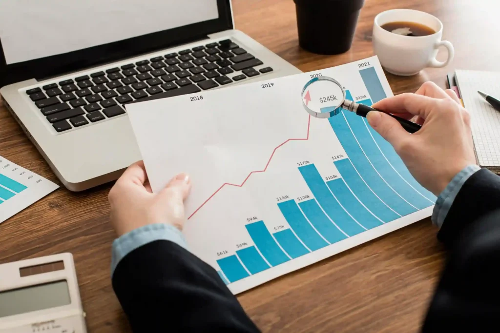 Pessoa analisando gráfico de barras e linha de tendência com lupa, representando o uso de dados históricos na análise de sazonalidade JoomPulse para a Copa do Mundo