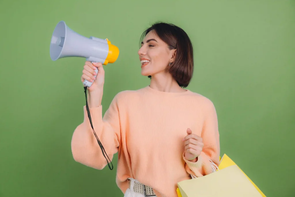 Mulher usando megafone e segurando sacolas de compras, representando estratégias para chamar atenção no marketplace