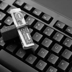 Teclado de computador com nota de dólar presa por cadeado, simbolizando bloqueio de valores em transações digitais