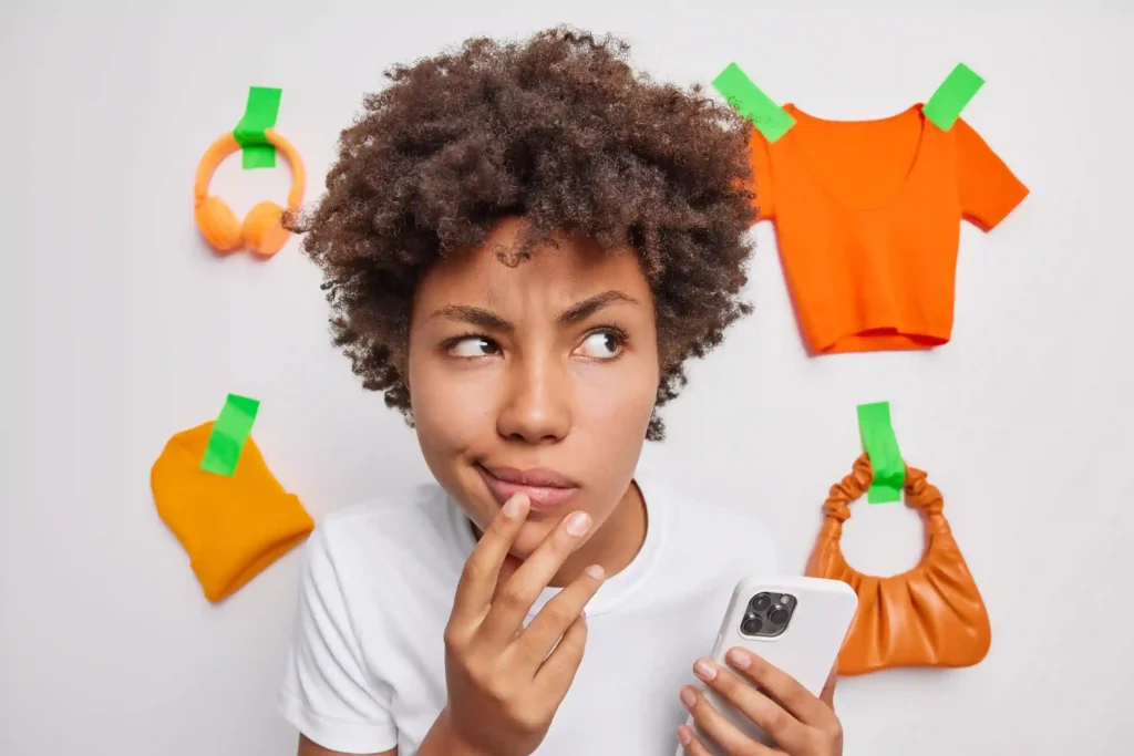 Mulher pensativa com smartphone rodeada de produtos fixados na parede, ilustrando o comportamento do consumidor pós-evento e a jornada de decisão de compra