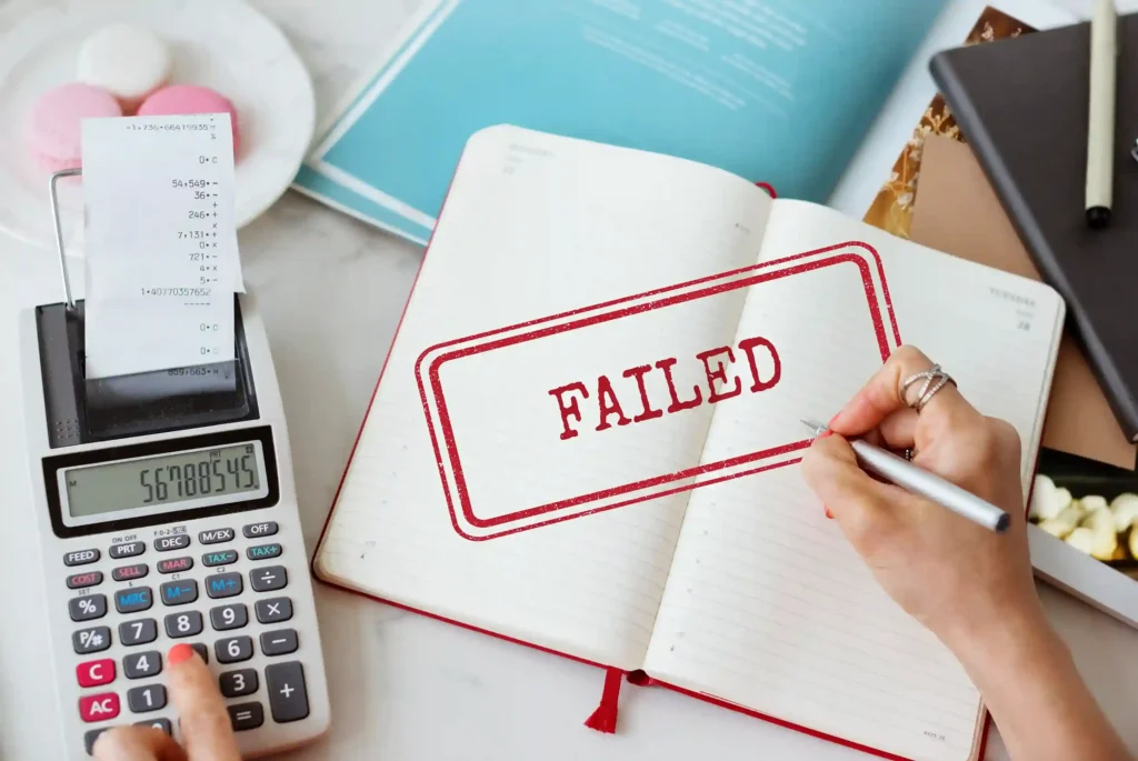 Mesa de trabalho com calculadora imprimindo recibo e caderno aberto com carimbo vermelho “FAILED”, simbolizando perda financeira