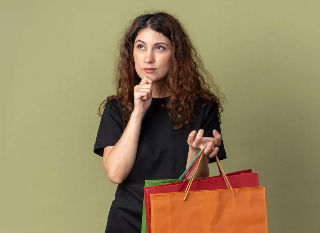 Pessoa de camiseta preta segurando sacolas coloridas e fazendo gesto pensativo, representando decisão de compra