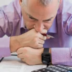 Homem preocupado analisando contas e calculadora, representando taxas invisíveis que reduzem a margem no e-commerce