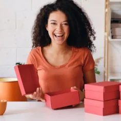 Empreendedora animada organizando caixas de produto rosa, representando a preparação do estoque dia das mães 2026