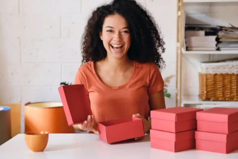Empreendedora animada organizando caixas de produto rosa, representando a preparação do estoque dia das mães 2026