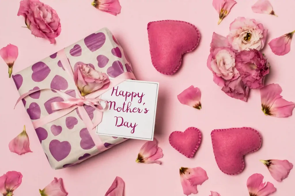 Presente embrulhado com papel estampado de corações roxos, laço rosa e cartão Happy Mother's Day rodeado de flores e corações de feltro sobre fundo rosa, ilustrando kit dia das mães para vender no Mercado Livre
