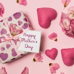 Presente embrulhado com papel estampado de corações roxos, laço rosa e cartão Happy Mother's Day rodeado de flores e corações de feltro sobre fundo rosa, ilustrando kit dia das mães para vender no Mercado Livre