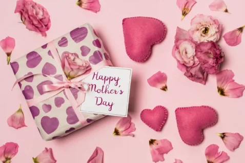 Presente embrulhado com papel estampado de corações roxos, laço rosa e cartão Happy Mother's Day rodeado de flores e corações de feltro sobre fundo rosa, ilustrando kit dia das mães para vender no Mercado Livre