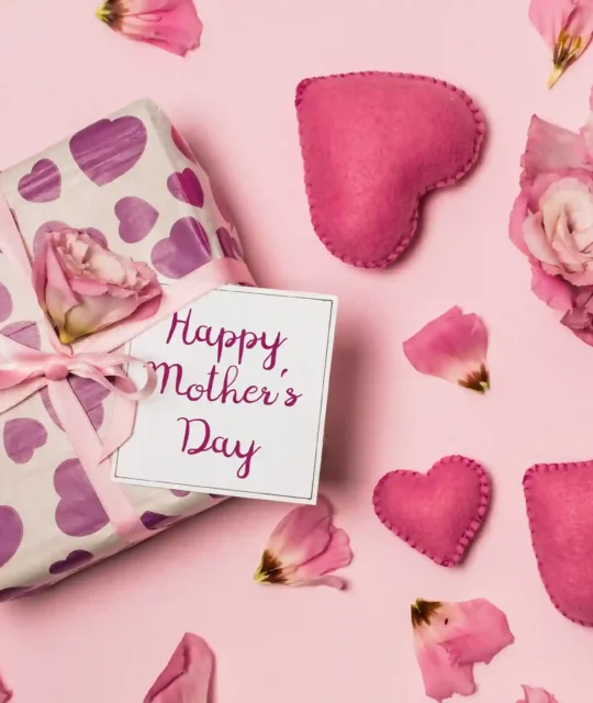 Presente embrulhado com papel estampado de corações roxos, laço rosa e cartão Happy Mother's Day rodeado de flores e corações de feltro sobre fundo rosa, ilustrando kit dia das mães para vender no Mercado Livre