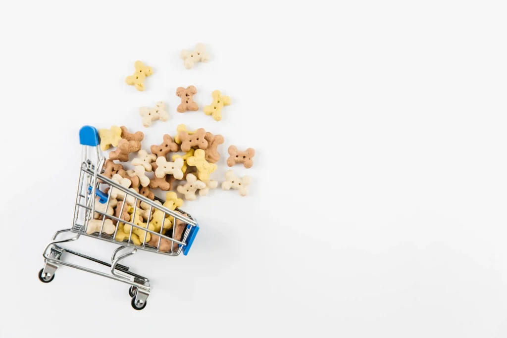 Carrinho de compras em miniatura transbordando petiscos em formato de osso, ilustrando o que vender no nicho pet online e a tendência de marketplaces com serviços digitais