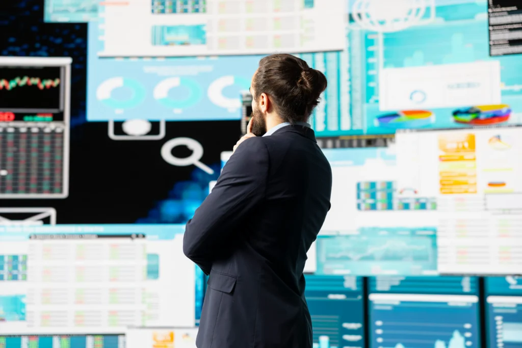 Homem de terno analisando múltiplos painéis de dados e gráficos em telas, ilustrando a análise estratégica para monitorar concorrentes no Mercado Livre