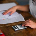 Pessoa usando calculadora com planilhas sobre a mesa, ilustrando a precificação no Mercado Livre para o Dia das Mães