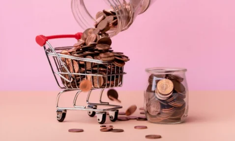 Carrinho de compras em miniatura cheio de moedas, com jarro despejando mais moedas, representando lucratividade no e-commerce